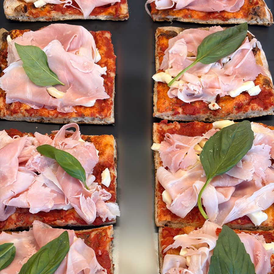 Parts de pizza romaine alla pala garnies de jambon et de basilic, en vitrine